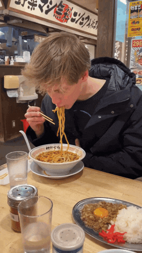 a man is eating noodles with chopsticks in front of a sign that says ' noodles ' on it