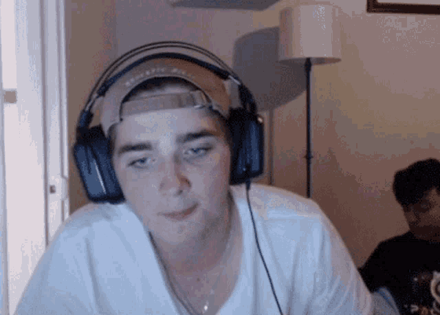 a young man wearing headphones and a baseball cap looks at the camera with his eyes closed