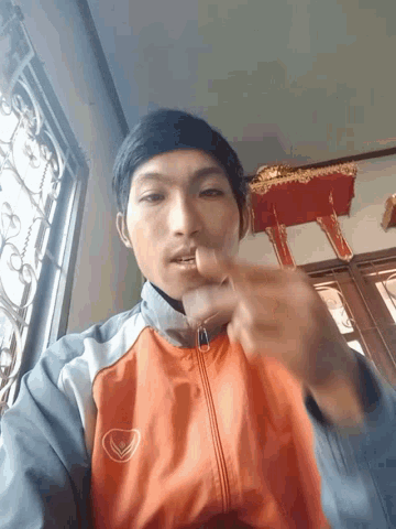 a man wearing an orange nike jacket is giving a middle finger