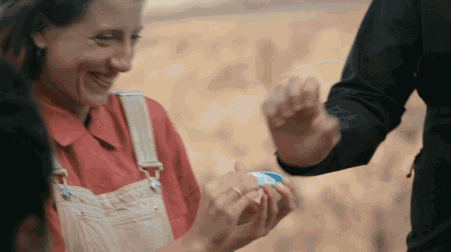 a woman wearing overalls is smiling while holding something in her hands