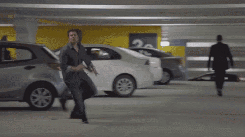 two men are running in a parking garage in front of a car .