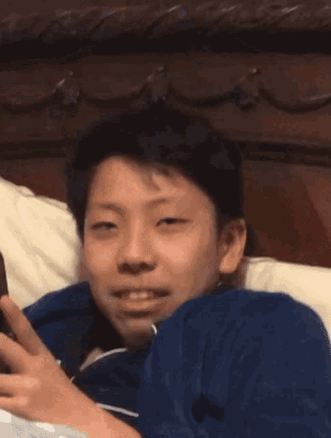a young boy is laying on a bed looking at his cell phone