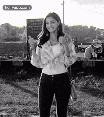 a black and white photo of a woman giving a thumbs up while standing in a field .