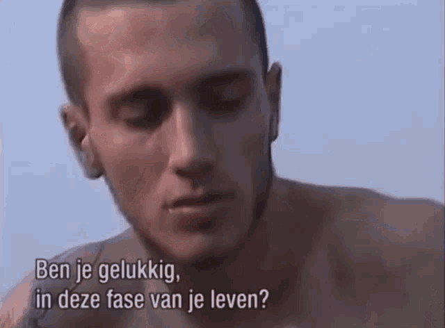 a man without a shirt is talking to another man in a video in a language other than english .