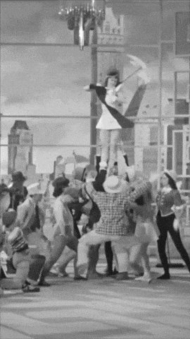 a black and white photo of a cheerleader being held up by people