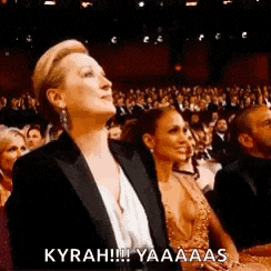 a woman in a tuxedo is sitting in front of a crowd at a awards show .