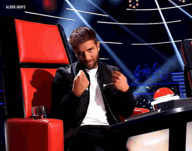 a man in a black jacket is sitting in a red chair with the words albor.ngifs on the bottom