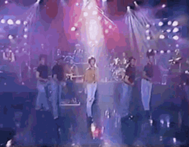 a group of people are standing on a stage in front of a stage with purple lights .