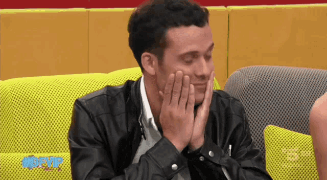 a man covering his face with his hands in front of a yellow couch that says #gfvip