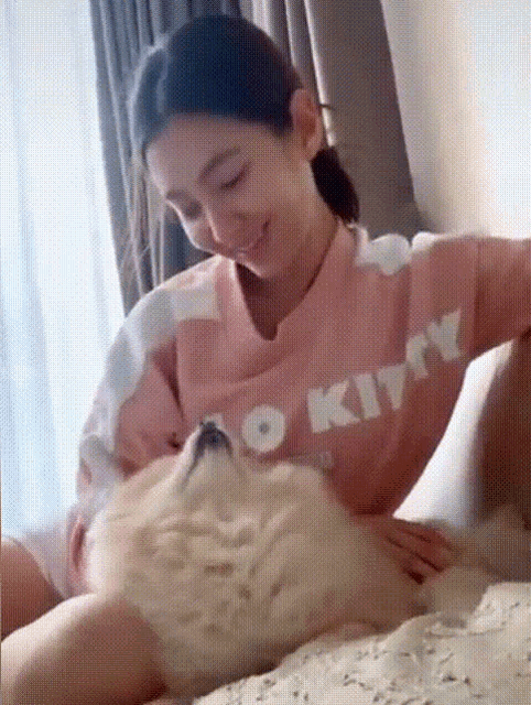 a woman wearing a pink hello kitty shirt is petting a dog