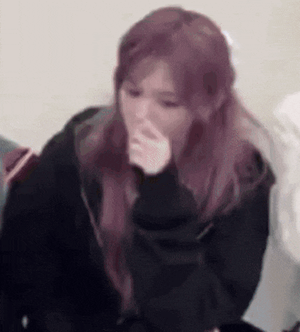 a girl with purple hair is covering her nose with her hand .