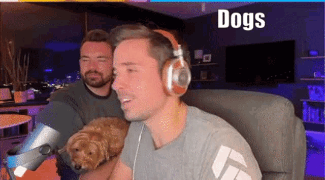 a man wearing headphones holds a small dog in his arms while another man looks on ..