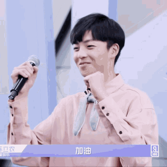 a young man in a pink shirt is holding a microphone and smiling with the number 9 on the bottom right