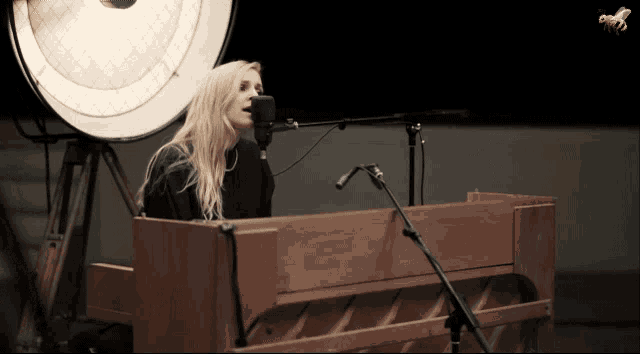 a woman singing into a microphone in front of a piano