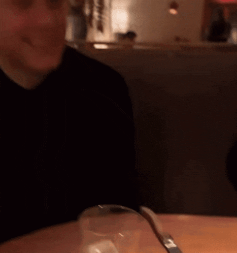 a man in a black shirt smiles while sitting in a dark room