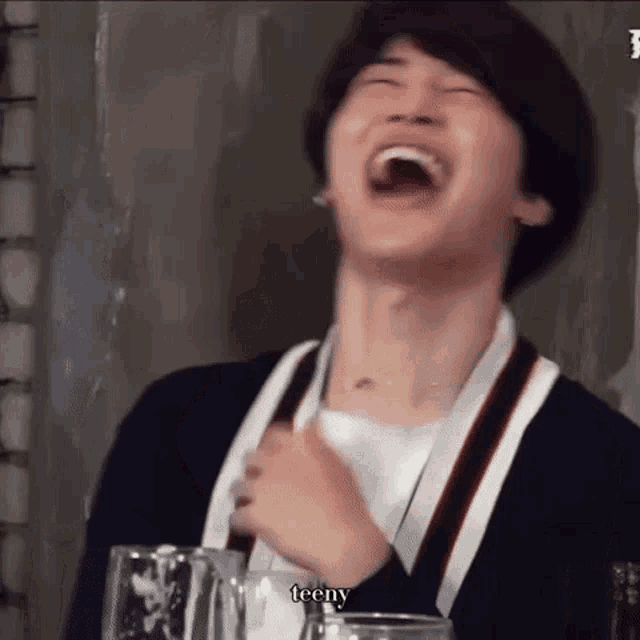 a young man is laughing with his mouth open and holding a glass of beer .