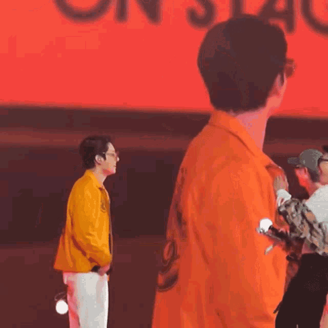 a man in an orange shirt is standing in front of a red background with the word on stage