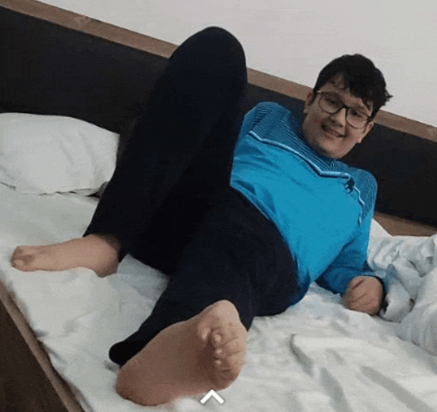 a boy wearing glasses and a blue shirt is laying on a bed with his legs crossed