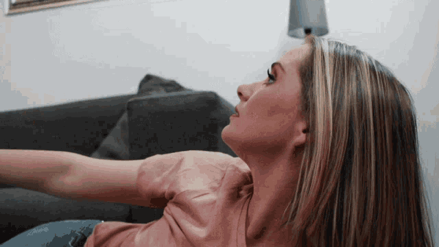 a woman in a pink shirt is laying on a grey couch