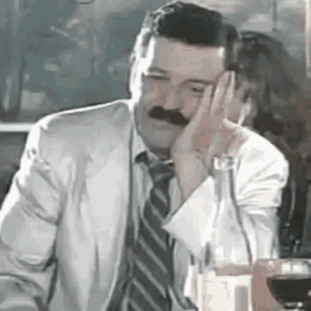 a man with a mustache is sitting at a table with a glass of wine .