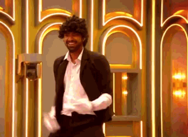 a man in a suit and white gloves is dancing in front of a wall with lights .