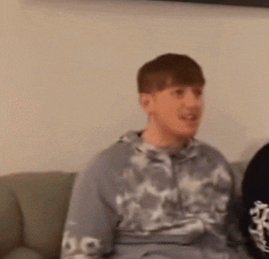 a young man is sitting on a couch wearing a tie dye hoodie .