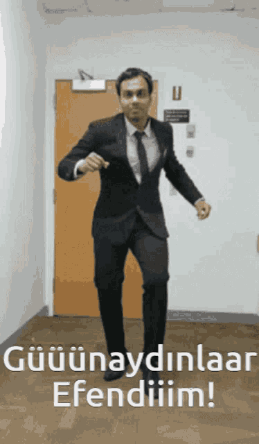 a man in a suit and tie is dancing in front of a door that says " gülunaydinlaar efendiim "