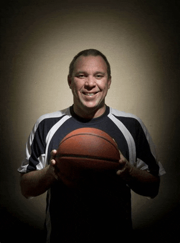 a man is holding a basketball in his hands and smiling for the camera