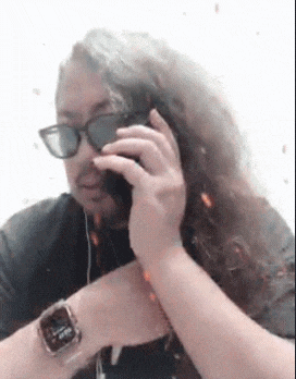 a man with long hair is talking on a cell phone while wearing sunglasses and a watch .