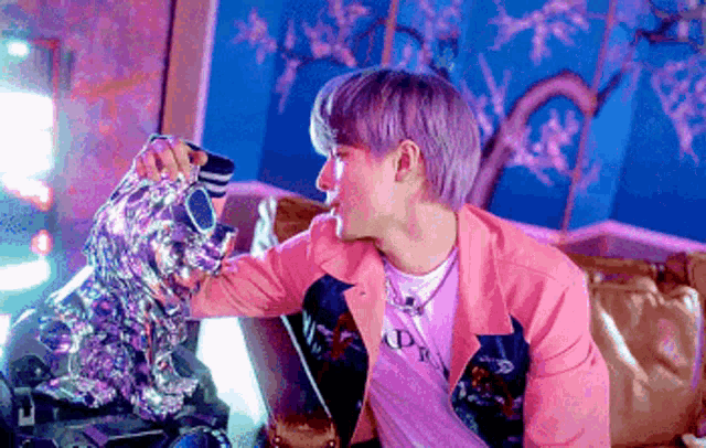 a man in a pink jacket is sitting on a couch petting a statue of a lion .
