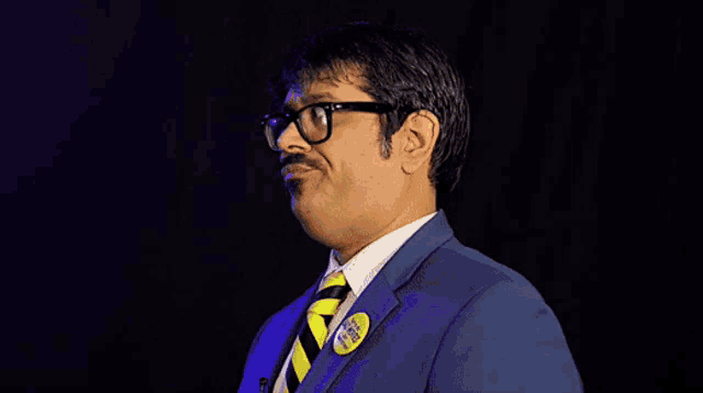 a man wearing glasses and a blue suit has a yellow badge on his jacket that says i 'm not a racist