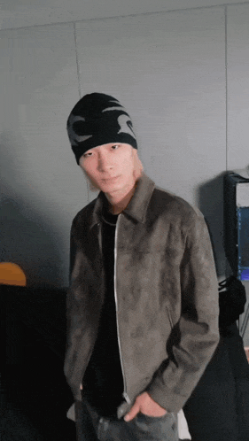 a man wearing a beanie and a jacket is standing in front of a wall