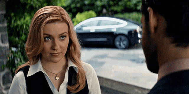 a man and a woman are looking at each other in front of a tesla model 3 car .