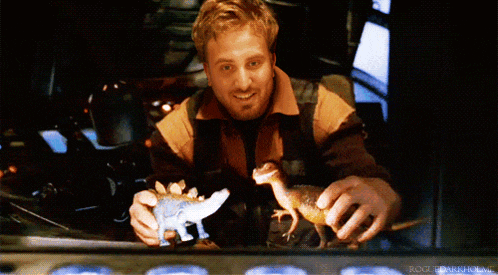 a man is holding a toy dinosaur and smiling in front of a window