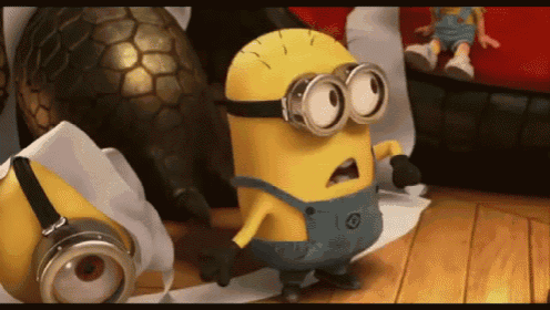 a yellow minion wearing overalls and goggles stands on a wooden floor