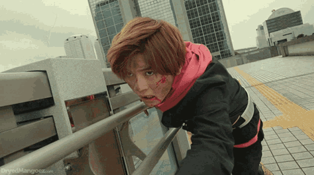 a man with blood on his face is standing next to a railing with the website dryedmango.com visible in the corner