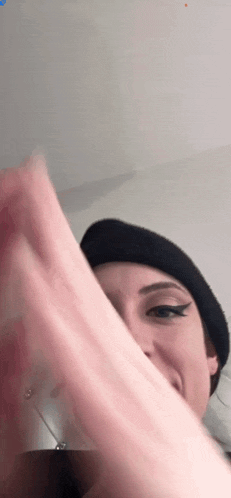 a woman wearing a black hat is covering her face with her hands .