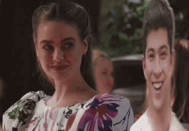 a woman in a floral dress stands in front of a cardboard cutout of a man
