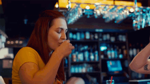 a woman in a yellow shirt is sitting at a bar drinking a drink