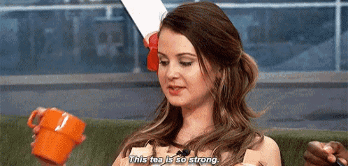 a woman is sitting on a couch holding a cup of tea and saying `` this tea is so strong . ''