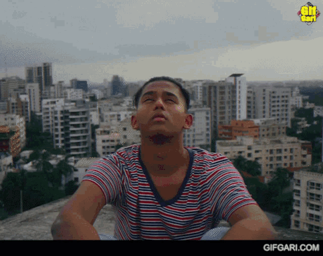 a man sitting on a rooftop with a city in the background and a gifgari.com logo