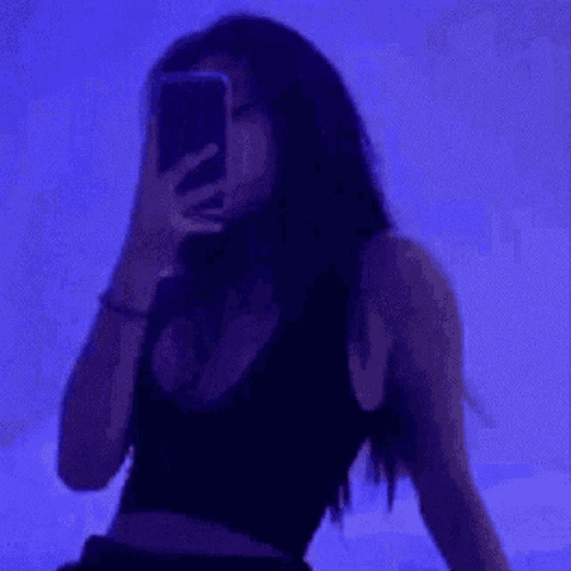 a woman is taking a selfie with her cell phone in a dark room with blue lights .