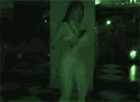 a woman is standing in front of a mirror in a dark room with a green light behind her .