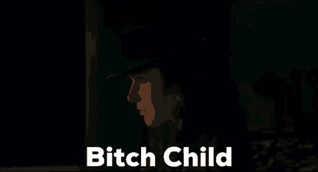a woman in a hat is standing in a dark room with the words `` bitch child '' written on the screen .