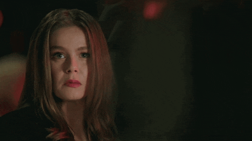 a woman with red hair is looking at the camera in a dark room