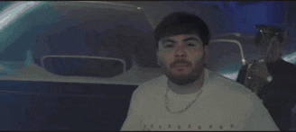a man with a beard is standing in front of a car and singing .