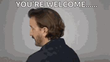 a man with long hair and a beard is standing in front of a gray background and says `` you 're welcome '' .