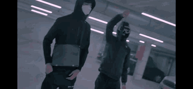 a man wearing a mask stands next to another man in a parking garage