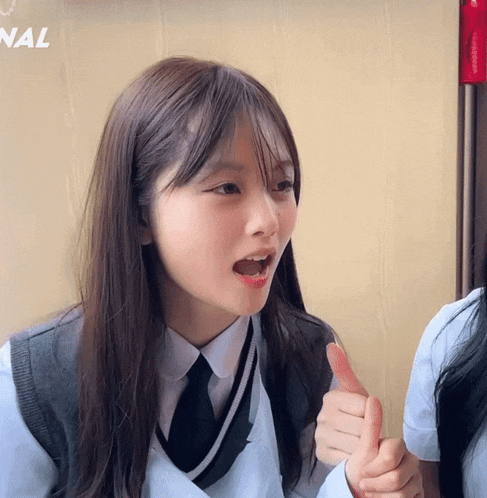 a girl gives a thumbs up in front of a wall that says nal
