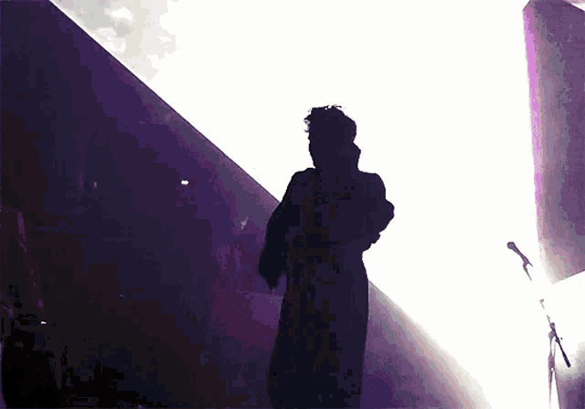 a silhouette of a man standing in front of a microphone in a dark room